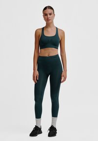 Atletische set met een donkergroene sportbeha en bijpassende leggings. De beha heeft een gladde afwerking en de leggings tonen getextureerde accenten.