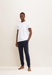 T-shirt en coton blanc avec une poche sur la poitrine, associé à un pantalon bleu marine à coupe décontractée, présentant des poignets côtelés et une texture lisse.