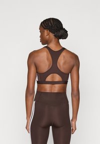 Καφέ αθλητικό σουτιέν με σχέδιο racerback, που διαθέτει άνοιγμα στο πίσω μέρος. Ομαλή υφή με αντίθετες λευκές πλευρικές λεπτομέρειες.