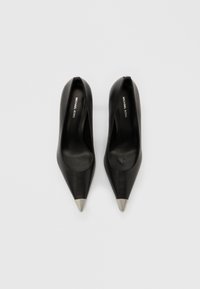 Czarne skórzane czółenka na wysokim obcasie, z zaostrzonym noskiem i metalicznym srebrnym zakończeniem. Gładka tekstura, zakładane bez zapięcia, z minimalistycznym logo wewnątrz.