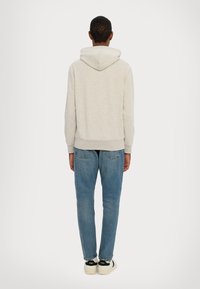 Světle šedá mikina s velkou kapucí, raglánovými rukávy a žebrovanými manžetami, ve spojení s modrými džínami a černými teniskami s bílými detaily.