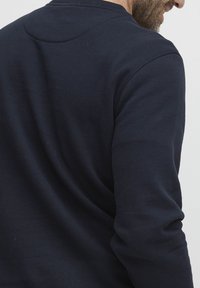 Tmavě námořnická bavlněná mikina s kulatým výstřihem, s hladkou texturou, žebrovanými manžetami a drobným detailem na ramenním švu.