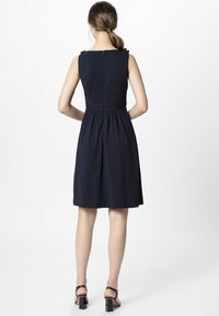 Navy sleeveless dress with ruffled shoulder accents, cinched waist, and flared skirt. Pair of black block-heeled sandals completes the look.