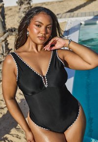 Maillot de bain noir une pièce avec un décolleté en V profond, un bord décoratif blanc le long des bords et un détail découpé au niveau de la poitrine. Tissu lisse et brillant.