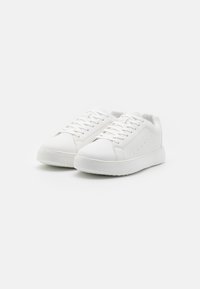 Sneaker bianche in pelle liscia con punta rotonda, dotate di lacci, minimalistiche perforazioni laterali e una suola in gomma chunky.