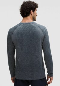 Dlhý rukáv šedá košeľa s textúrovaným pleteným dizajnom, rebrovaným golierom a spustenými plecami, s tmavými a svetlými farebnými variáciami.