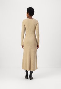 Vestito lungo beige a costine con maniche lunghe e collo rotondo, che arriva fino alla caviglia. Indossato con stivali neri con tacco al ginocchio.