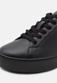 Baskets en cuir noir avec bout arrondi, design à lacets plats, semelle plateforme et semelle extérieure en caoutchouc texturé. Couture détaillée visible.