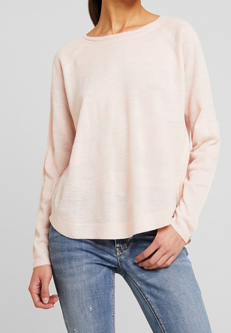 Hellrosa gestrickter Pullover mit lockerem Sitz. Verfügt über strukturierte horizontale Streifen und lange Ärmel, kombiniert mit blauen Jeans.