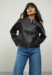 Zwarte leren cropped leren jas met een grote kraag en een rits aan de voorkant, gecombineerd met hoge taille blauwe denim jeans. Gladde textuur en een getailleerd ontwerp.