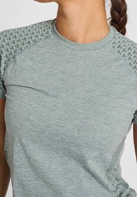 Szaro-zielona sportowa koszulka z krótkim rękawem, z fakturowanym wzorem na ramionach i gładką tkaniną na ciele. Okrągły dekolt i dopasowany krój.