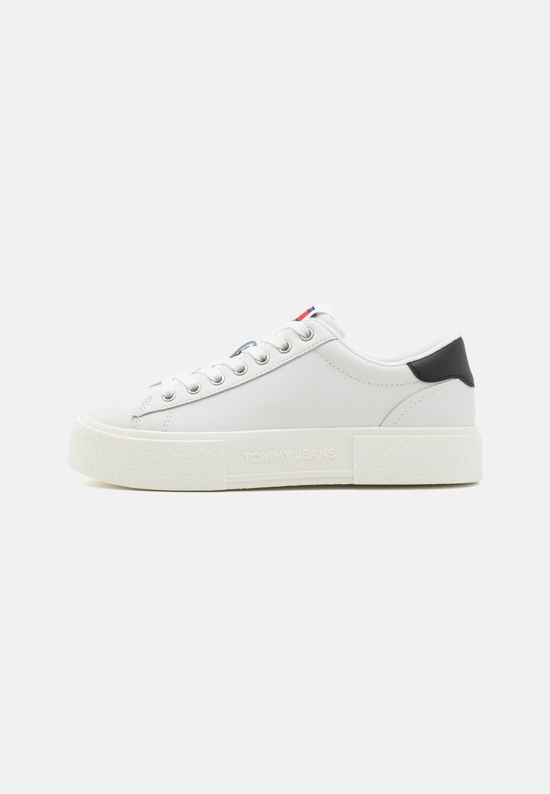 Zapatillas de cuero blancas con una suela de goma blanca texturizada, que cuentan con una copa de talón negra y acentos en azul/blanco/rojo en la lengüeta. Logo de "TOMMY JEANS".