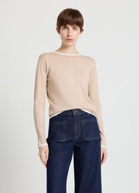 Light beige knit sweater with a crew neck and white trim, paired with dark blue high-waisted jeans featuring two back pockets.