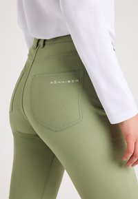 Gröna tajta byxor gjorda av stretchigt material med bakfickor och synlig sömnad. Logotypen "Röhnisch" broderad på den högra fickan.