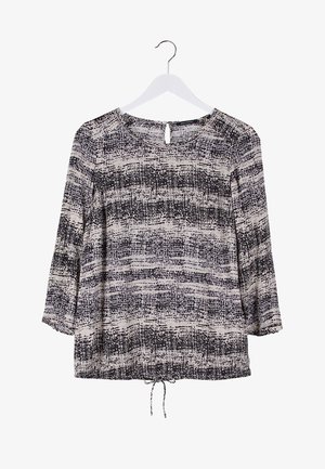 Vrouw die een zwart-wit top met lange mouwen draagt met een patroon, gescheurde skinny jeans, zwarte enkellaarsjes en een kleine beige handtas vasthoudt.