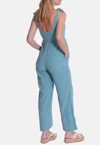 Helles blaues, geripptes Jumpsuit mit verstellbaren Bindeträgern, Seitentaschen und lockerer Passform. Tragen mit beigen Espadrilles.