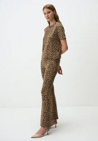 Completo maculato di leopardo in marrone e beige, composto da una maglietta a maniche corte e pantaloni svasati, realizzato in tessuto morbido, abbinato a tacchi beige.