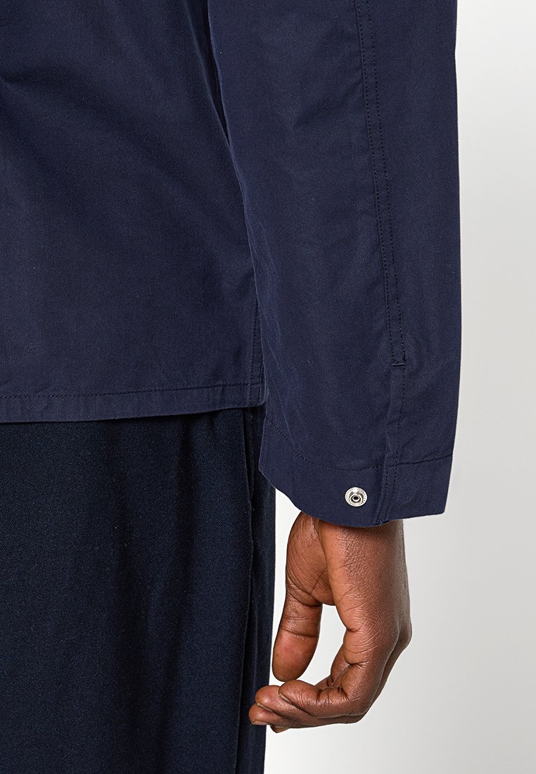 Camisa de manga larga azul marino con un detalle de botón en el puño, hecha de tela suave, con un corte recto y costuras mínimas.