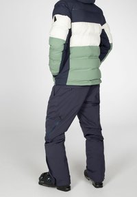 Padded jacket in navy blue, white, and mint green; features horizontal stripes, zippered pockets; paired with dark navy pants and black ski boots.