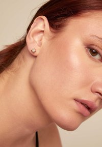 Boucles d'oreilles en or avec un design floral comportant de petites pierres précieuses transparentes. Surface en métal lisse, forme compacte, adaptées à un usage quotidien.