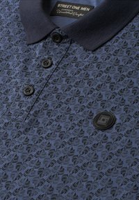 Polo homme bleu foncé à motif avec boutons noirs et écusson rond noir avec logo sur la poitrine, col côtelé.