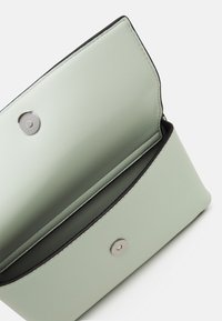 Portfel z zielonej mięty wykonany ze skóry, z zapięciem na zatrzask, charakteryzujący się gładką teksturą i czarnym akcentem na krawędzi. Wnętrze wyłożone jest miękką podszewką.