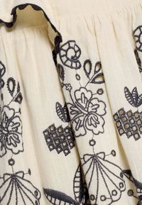 Cream fabric featuring intricate black floral embroidery, scalloped edges, and detailed patterns with openwork accents.