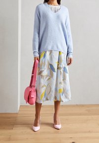 Jasnoniebieski, dzianinowy sweter z dekoltem w kształcie V; kwiatowa, midi spódnica w niebieskim, żółtym i beżowym kolorze; różowa torebka i jasnoróżowe szpilki.
