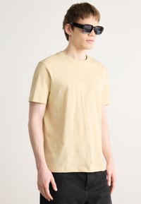 Lysegul bomulds t-shirt med rund hals og korte ærmer, parret med enkle, sorte solbriller med en kantet form. Simple og minimalistiske designfunktioner.