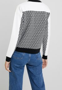 Maglione bianco e nero con un motivo geometrico sul retro, parte frontale completamente bianca e polsini e orlo a costine neri; vestibilità rilassata.