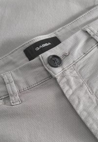 Pantalones Gabba grises con un acabado texturizado, que cuentan con una etiqueta negra, cierre de botón y costuras reforzadas en los bolsillos.