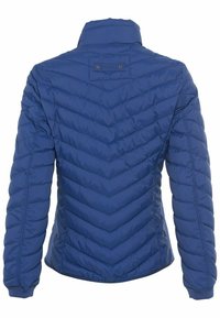 Sininen tikattu takki korkealla kauluksella, jossa on chevron-kuvio, joustavat hihansuut ja pieni logotagi takana.