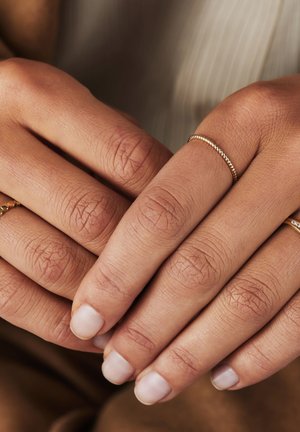 Goldringe mit verdrehten und glatten Designs, die an Händen mit natürlichen, unpolierten Nägeln und strukturierter Haut getragen werden.