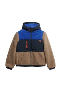 Vachtige beige en marineblauwe jas met een blauwe corduroy bovenkant, capuchon en oranje accenten. Voorzien van zippered zijzakken en een borstzak.