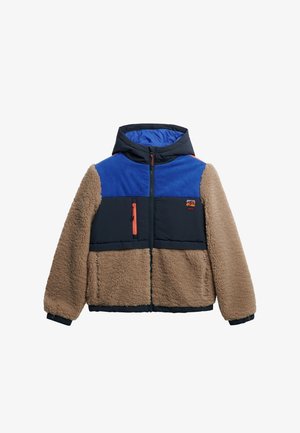 Vachtige beige en marineblauwe jas met een blauwe corduroy bovenkant, capuchon en oranje accenten. Voorzien van zippered zijzakken en een borstzak.