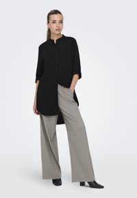 Camicia nera a maniche lunghe con chiusura a bottoni, orlo asimmetrico. Abbinata a pantaloni a gamba larga grigio chiaro e stivaletti neri con tacco.