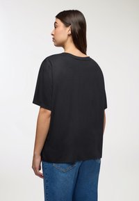 Czarna bawełniana koszulka z luźnym krojem, krótkimi rękawami i okrągłym dekoltem. Gładka tekstura i lekko wydłużony tylny brzeg.