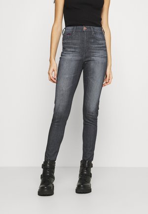 Vaqueros pitillo de talle alto en denim gris oscuro. Cuenta con cinco bolsillos, trabillas para cinturón y detalles sutiles de costura. Combinados con botines negros.