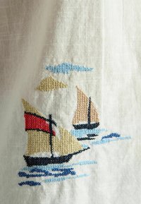 Two sailboats with beige and red sails embroidered on white fabric, with blue waves and a blue cloud above.