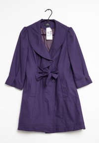 Lila damrock med bred krage, trekvartslånga ärmar, två framfickor, knapppropp och en knytbälte som hänger på en svart galge.