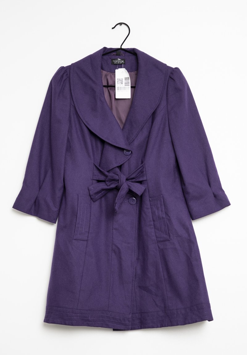 Lila damrock med bred krage, trekvartslånga ärmar, två framfickor, knapppropp och en knytbälte som hänger på en svart galge.