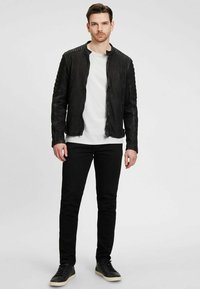 Zwarte leren jas met gestructureerde schouderdetails, voorkeursrits, gecombineerd met een wit shirt, zwarte jeans en donkere sneakers.