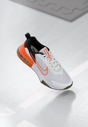 Weißer und oranger Nike Air Max Sneaker mit sichtbarem Luftkissen, Mesh-Obermaterial und Schnürdesign, schwebt über einer hellgrauen Oberfläche.