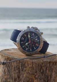 Reloj cronógrafo Nautica con caja de acero inoxidable plateado, correa de silicona azul marino, esfera negra texturizada y detalles en rojo, blanco y azul.