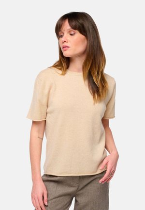 Pull beige en maille à manches courtes avec un col rond. Texture douce et coupe décontractée, associé à un pantalon à carreaux.