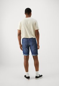 Jeansshorts med uppvikta kantar, mörkblå färg, med en klassisk femfickadesign. I kombination med en ljusbeige t-shirt och svarta sneakers.