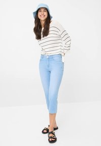 Jeans cropped bleu clair avec un design ajusté ; associées à un haut rayé blanc et un chapeau seau bleu. Sandales noires avec des accents de boucle.