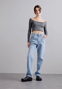 Gray off-the-shoulder ribbed top paired with light blue high-waisted jeans and black chunky shoes, set against a neutral background.