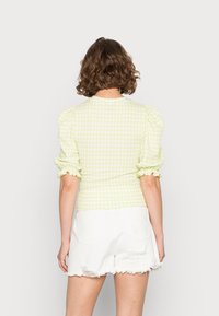 Top amarelo de gingham com mangas bufantes e punhos franzidos, combinado com calções brancos desgastados. O tecido parece leve e texturizado.