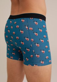 Modré trenýrky s černým páskem mají opakující se vzor karikatury vzpěrače v červené, růžové a černé barvě, vyrobené z elastického materiálu.